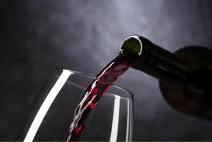 Vino tinto siendo servido desde una botella en una copa de cristal, con fondo oscuro y elegante.