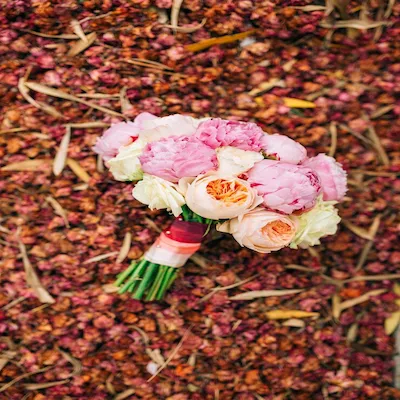 Ramo de flores rosas y durazno sobre un fondo de pétalos secos y hojas caídas, capturado desde arriba.